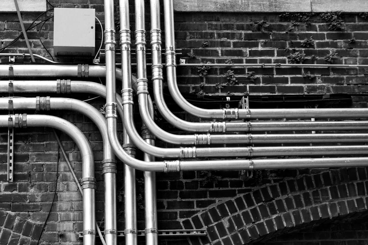 Black and white image of industrial stainless steel pipes mounted on a brick wall.